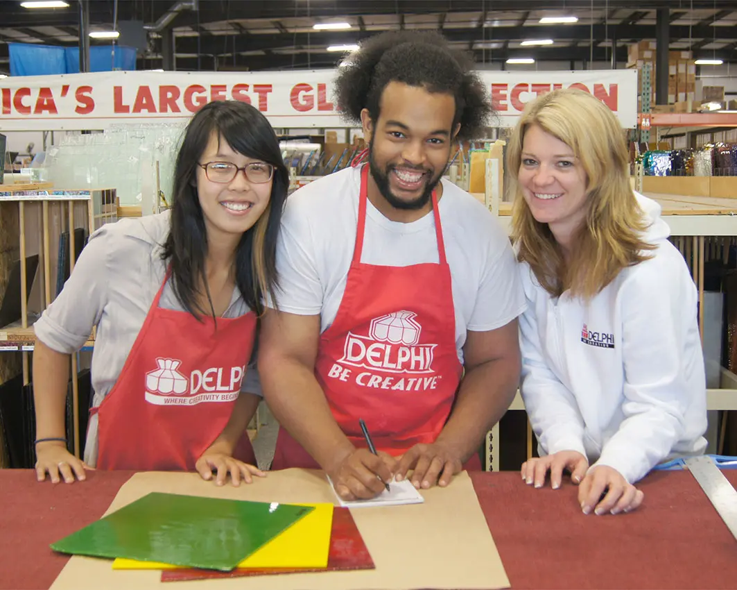 Three Delphi Glass team members smiling at a cutting table in the Delphi Glass warehouse